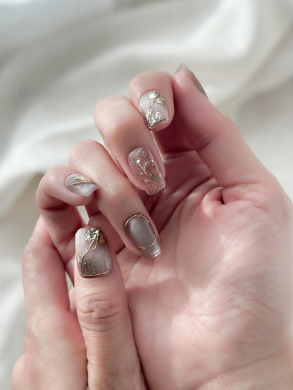Close-up of hands with nude and taupe press-on nails with gold foil accents, rose gold glitter, and marble details